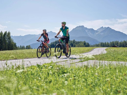 Herzlich willkommen in unserem Hotel in Matrei am Brenner Zwei Radfahrer fahren auf Landstraße mit Bergen und Wiesen im Hintergrund