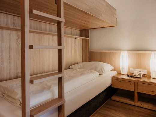 The perfect hotel for group travel in Tyrol Single bed with wooden bunk ladder and bedside table with phone and lamps