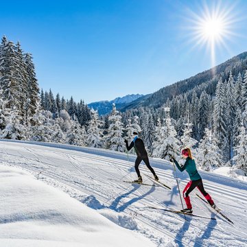Neuigkeiten aus dem Motorradhotel in Tirol Zwei Menschen beim Langlaufen im sonnigen verschneiten Wald