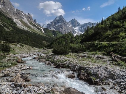 Hiking in Matrei am Brenner Mountain stream flowing through a valley with green slopes and snow-capped peaks