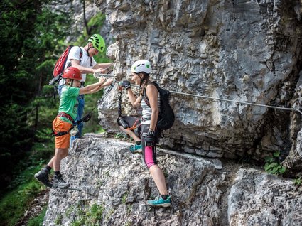 Holidays at the Brenner Pass: hiking and climbing Three people climbing a rock wall wearing helmets and using climbing gear