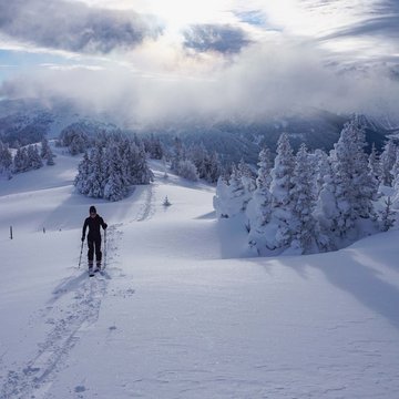 Neuigkeiten aus dem Motorradhotel in Tirol Skifahrer wandert durch verschneite Berglandschaft unter bewölktem Himmel